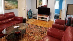 A living room with a red leather sofa, a glass coffee table, a TV on a wooden stand, and a patterned rug. - Monthly winter rates. Ground floor. Heart of Surf City. 515 N. Shore Dr. Apt. #3 (Surf City)