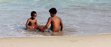 Twee kinderen spelen in ondiep water in de buurt van een zandstrand.