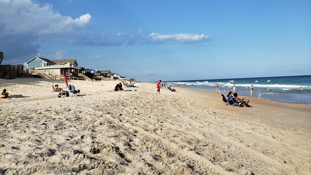 A sandy beach with beach chairs, umbrellas, and a few people. There are houses in the background. - Monthly winter rates. Ground floor. Heart of Surf City. 515 N. Shore Dr. Apt. #3 (Surf City)
