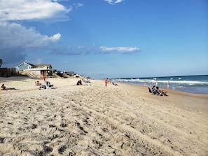 A sandy beach with beach chairs, umbrellas, and a few people. There are houses in the background. - Monthly winter rates. Ground floor. Heart of Surf City. 515 N. Shore Dr. Apt. #3 (Surf City)