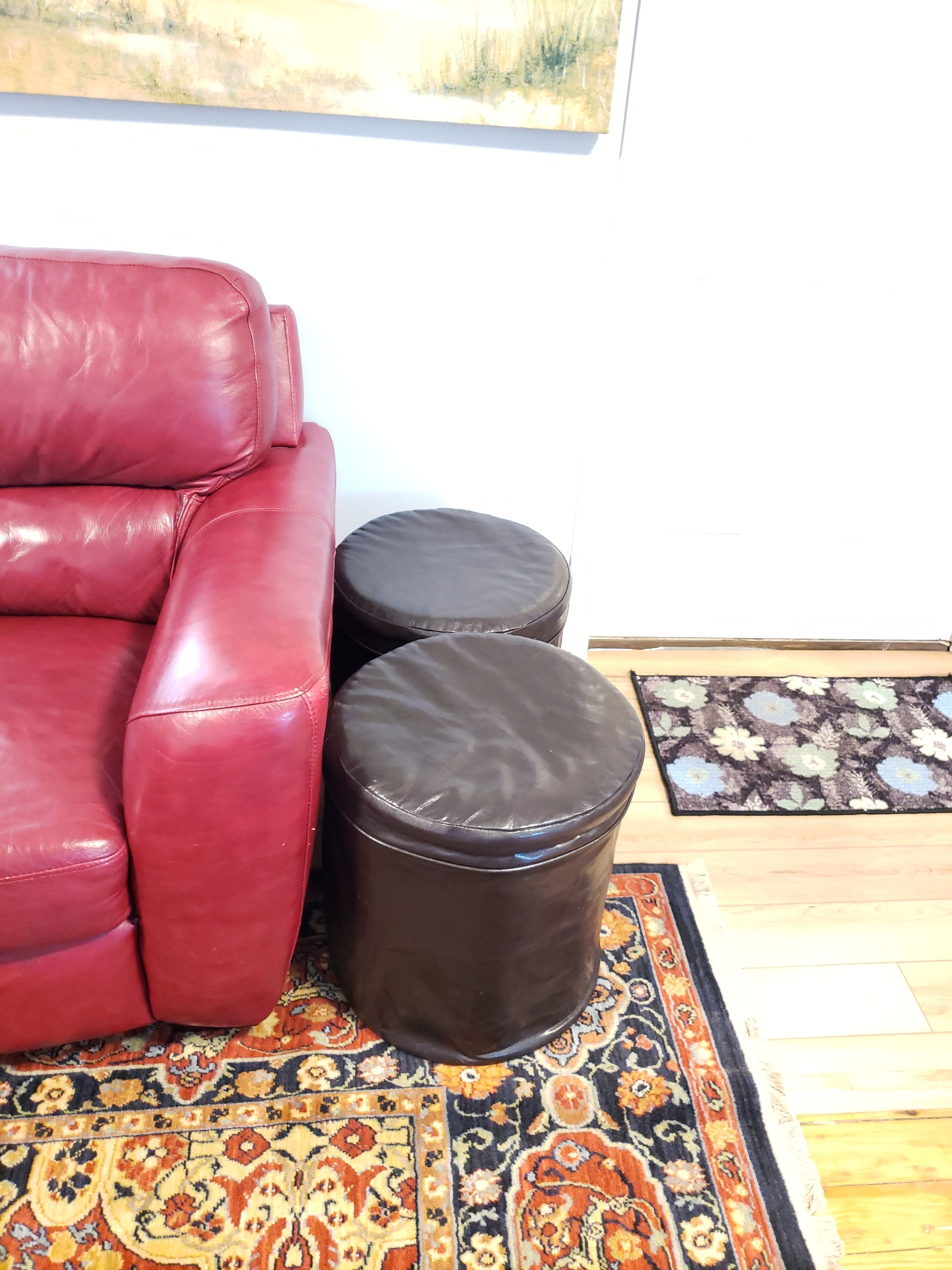 A red leather sofa and two round ottomans on a patterned rug.