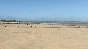 A wide sandy beach with a series of black bollards and a clear sky.