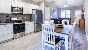 Een moderne keuken met witte kastjes, roestvrijstalen apparatuur en een eethoek met een houten tafel en witte stoelen.
