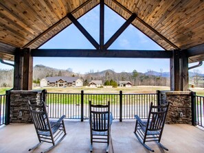 Une terrasse couverte avec trois fauteuils à bascule, un mur en pierre et une vue sur des maisons et des montagnes.