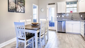 Een moderne keuken met witte kasten, een roestvrijstalen vaatwasser en een eethoek met witte stoelen en een houten tafel.