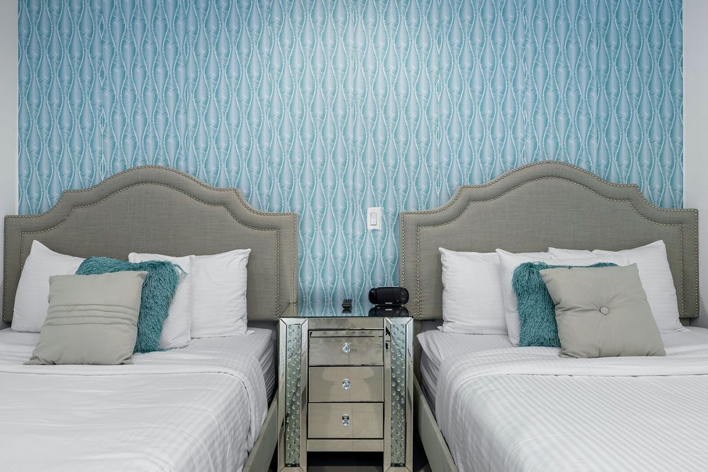 Habitación de hotel con dos camas, una mesita de noche y un papel tapiz estampado.