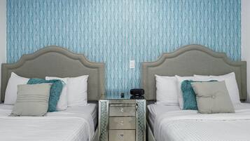 Habitación de hotel con dos camas, una mesita de noche y un papel tapiz estampado.
