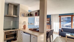 A compact kitchen with modern appliances, a dining area with a table and chairs, and a cozy living space with a sofa and a bookshelf. - APARTMENT WITH POOL ACCESS - ST JEAN D'AULPS RESORT - 6 Pers / 60m² - Riam D2 (Saint-Jean-d´Aulps)