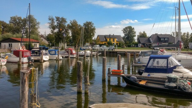 A marina with boats docked, wooden pilings, and a yellow building in the background. - Vacation home Bodden - semi-detached house (Saal)