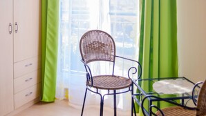 A room with a wicker chair, a glass table, a green curtain, and a white wardrobe. - Vacation home Bodden - semi-detached house (Saal)