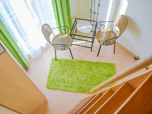 A room with a staircase, a green rug, and two wicker chairs around a small table.