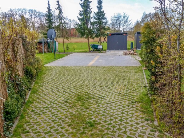 A paved courtyard with a green lawn, a metal fence, and a small shed.