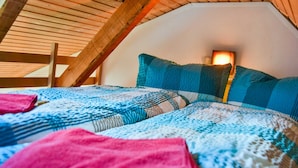 A bedroom with a sloped ceiling, wooden beams, a bed with patterned bedding, and a bedside lamp. - Vacation home Bodden - semi-detached house (Saal)
