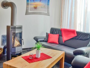 A living room with a black leather sofa, red cushions, a wooden coffee table, a glass vase with a plant, and a wood-burning stove.