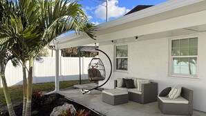 Ein überdachter Patio-Bereich mit Schaukelstuhl, zwei Sofas und einem Esstisch.