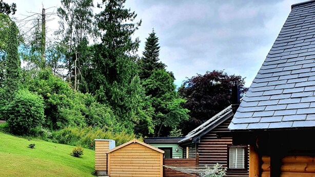 A log cabin with a sloped roof, surrounded by a well-maintained lawn and dense forest. - Luxury lodge (Blairgowrie)