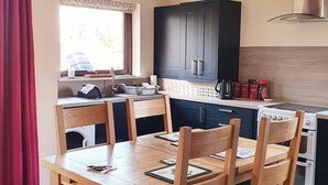 A compact kitchen with a dining table, wooden chairs, a stove, and cabinets. - Luxury lodge (Blairgowrie)
