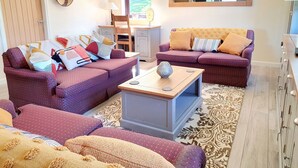 A living room with two sofas, a coffee table, and a dining area with a chair and table. - Luxury lodge (Blairgowrie)