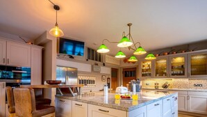 Una cocina moderna con gabinetes blancos, una isla grande y lámparas colgantes verdes.