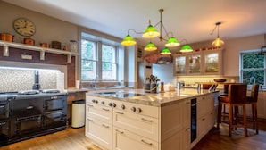 Una cocina moderna con una isla central, estufa y lavamanos. Hay varias luces colgantes y un reloj en la pared.