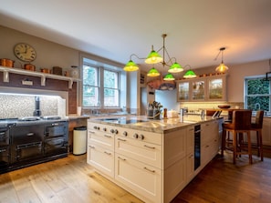 A modern kitchen with a central island, a stove, and a sink. There are multiple hanging lights and a clock on the wall.