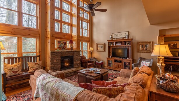 A cozy living room with a fireplace, large windows, a ceiling fan, and a television. - Mossy Path Hideaway - Blowing Rock area home with easy access and ping pong! (Blowing Rock)
