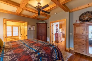 Ein schlicht eingerichtetes Schlafzimmer im Blockhausstil mit Holzboden, einem Bett mit gemustertem Überwurf, einem Holzschrank und einem Deckenventilator.