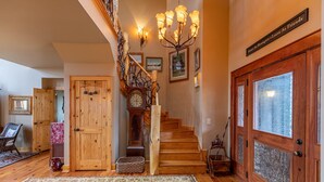 A wooden staircase with a chandelier, a large wooden door with frosted glass panels, and a rug on the floor. - Mossy Path Hideaway - Blowing Rock area home with easy access and ping pong! (Blowing Rock)