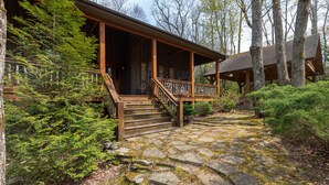 A rustic cabin with a stone-paved entrance, wooden deck, and a covered porch. - Mossy Path Hideaway - Blowing Rock area home with easy access and ping pong! (Blowing Rock)