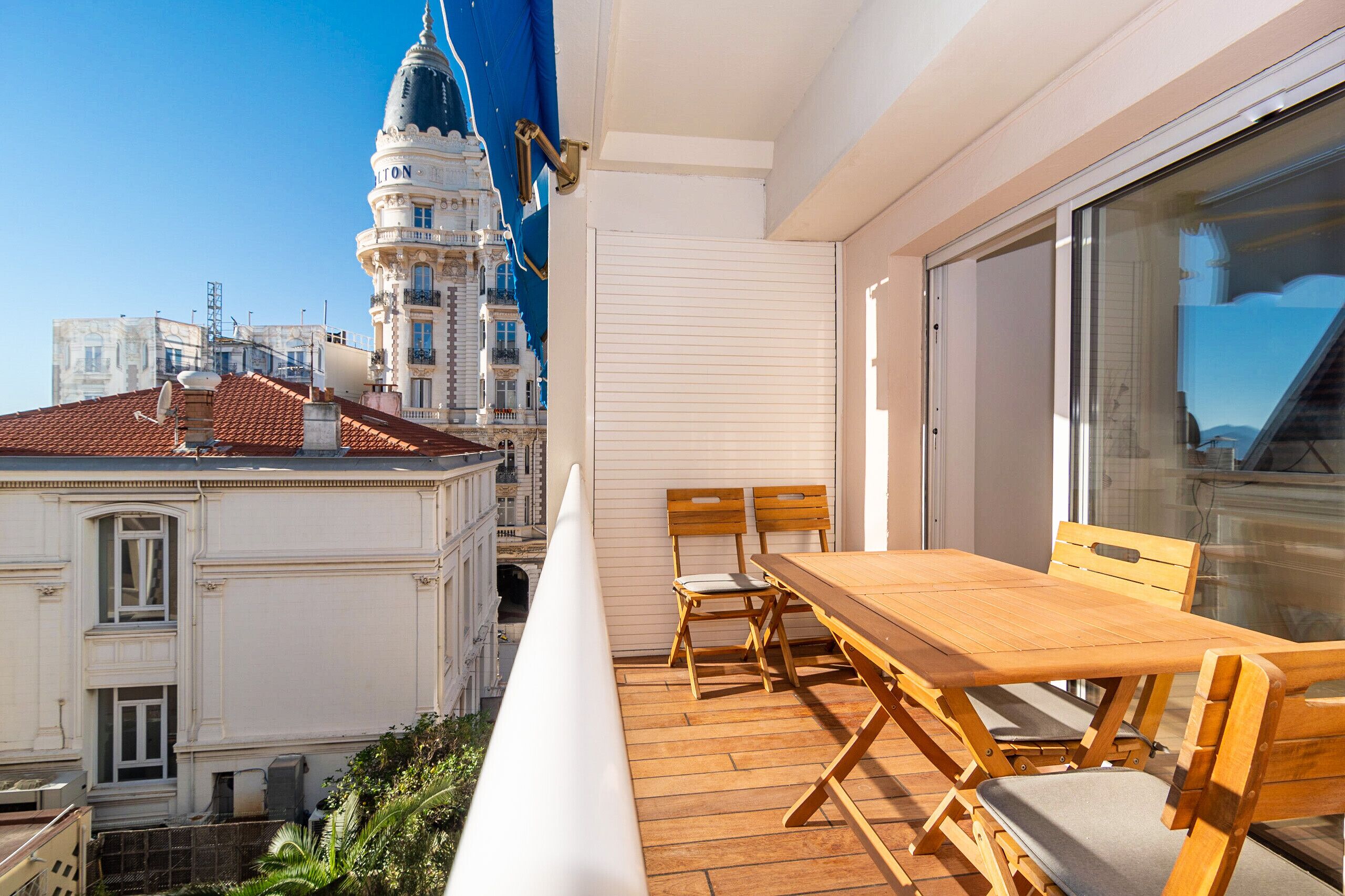 Ein Balkon mit Holztisch und -stühlen, der auf eine Stadtansicht mit historischen Gebäuden und einem Turm blickt.