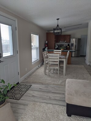 A modern kitchen with a stainless steel refrigerator, a dining area with a wooden table and chairs, and a carpeted floor. - Cheerful 2 bedroom 2 bath home in Sheridan. (Sheridan)