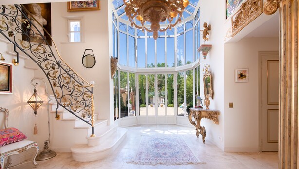 A grand staircase with ornate metalwork, a large chandelier, and a view through a glass door to an outdoor area.