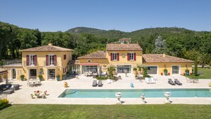 A two-story yellow villa with a swimming pool, outdoor seating, and a view of the surrounding hills.