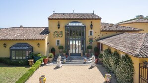 A yellow building with a tiled roof, a glass door, and potted plants.