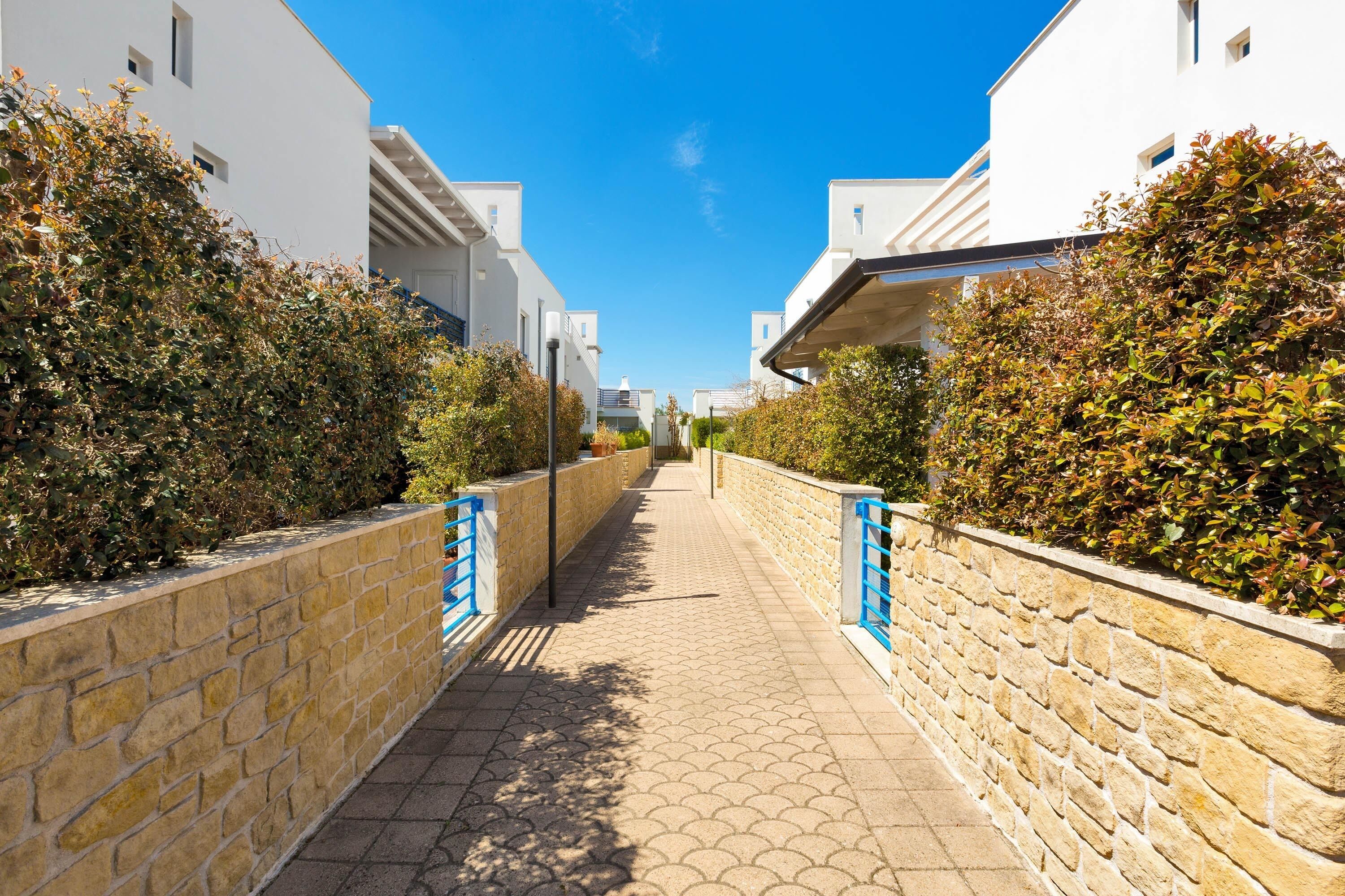 A pathway flanked by stone walls and white buildings with blue railings.