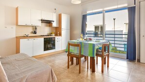 A compact kitchen with white cabinets, a stove, and a dining area with a table and chairs. - Appartamento Cristallo by BarbarHouse (Boncore)