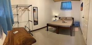 A bedroom with a bed, a bedside table, a hanging clothes rack, a mirror, and a window with curtains. - TamaKing & Beds (Tamarindo)