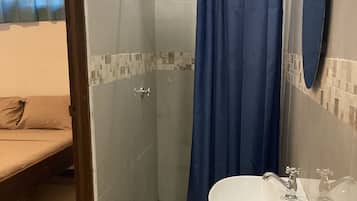 Een badkamer met een douchecabine van glas, een wastafel met spiegel en een bed zichtbaar door een geopende deur.