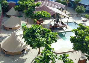 Un espace aménagé au bord de la piscine, comprenant des tentes, un coin salon couvert et une végétation luxuriante.
