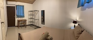Un dormitorio con cama, escritorio, silla, estante y lámpara.