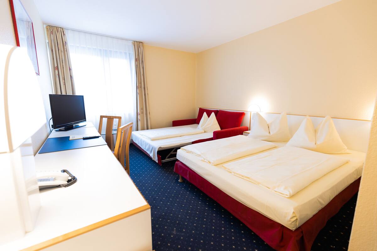 Ein Hotelzimmer mit zwei Betten, einem Schreibtisch mit Computer und einem Stuhl.