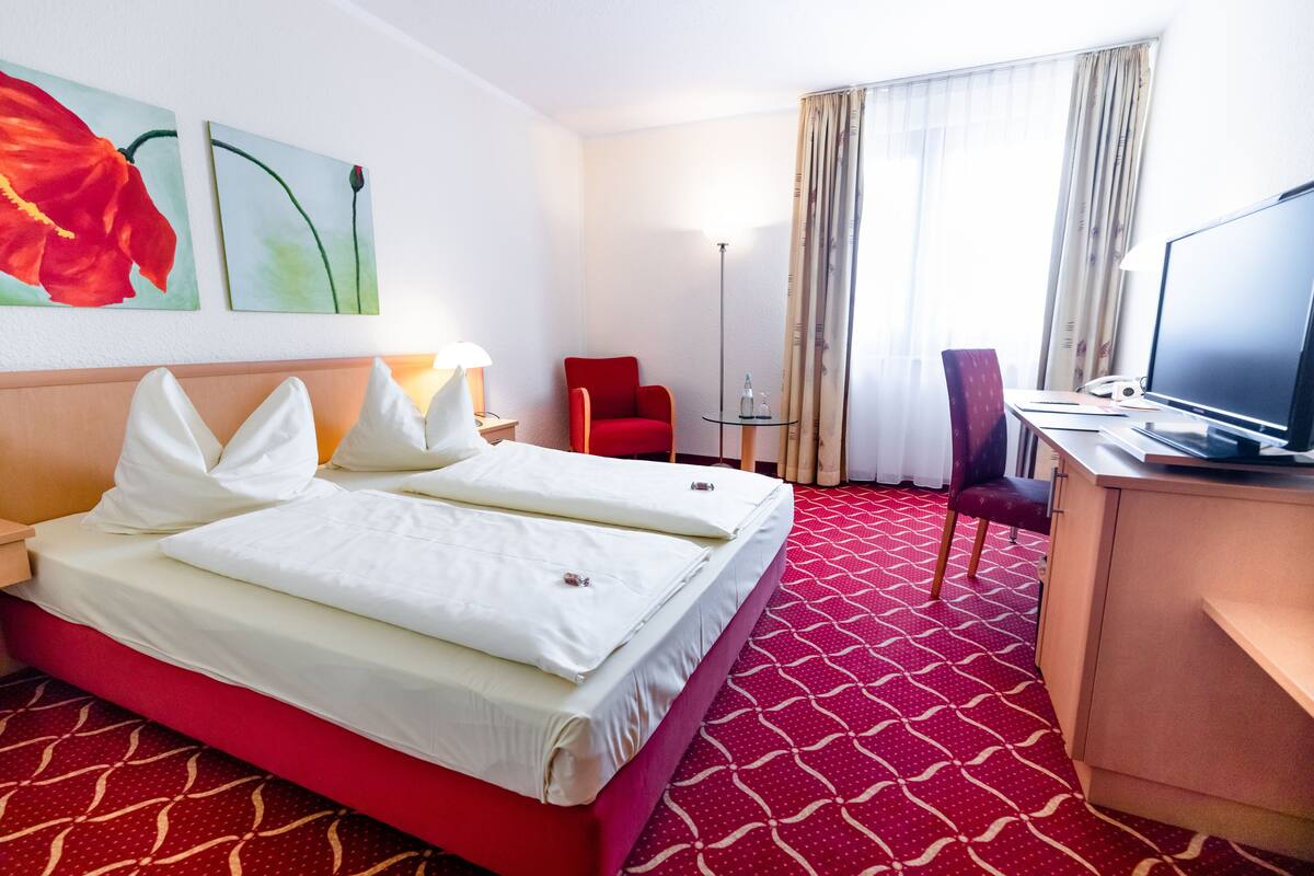 Ein Hotelzimmer mit einem Bett, einem Schreibtisch mit Computer, einem Sessel und einem Fernseher.