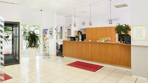 Ein heller, moderner Empfangsbereich mit einem Holzbüro, einer Zimmerpflanze und einer roten Fußmatte.