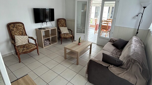 A living room with a sofa, two armchairs, a coffee table, a TV, and a sliding glass door leading to an outdoor area. - Comfortable house near town center and beaches (Jard-sur-Mer)
