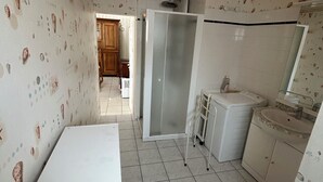 A small, compact kitchen with white cabinets, a white countertop, and a tiled floor. There is a white washing machine and a small sink with a mirror above it. - Comfortable house near town center and beaches (Jard-sur-Mer)