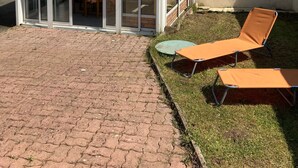 A covered patio area with a glass enclosure, two lounge chairs, and a brick pathway. - Comfortable house near town center and beaches (Jard-sur-Mer)