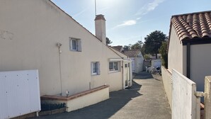 A narrow driveway leading to a residential building with a white exterior and a tiled roof. - Comfortable house near town center and beaches (Jard-sur-Mer)