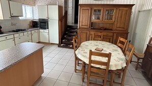 A kitchen with a dining table, cabinets, and a staircase leading to another room. - Comfortable house near town center and beaches (Jard-sur-Mer)