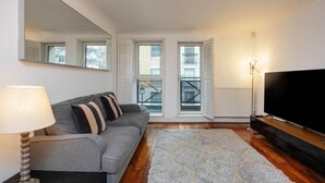A living room with a grey sofa, a lamp, a TV on a wooden stand, and a patterned rug. - At Home in Marylebone (London)
