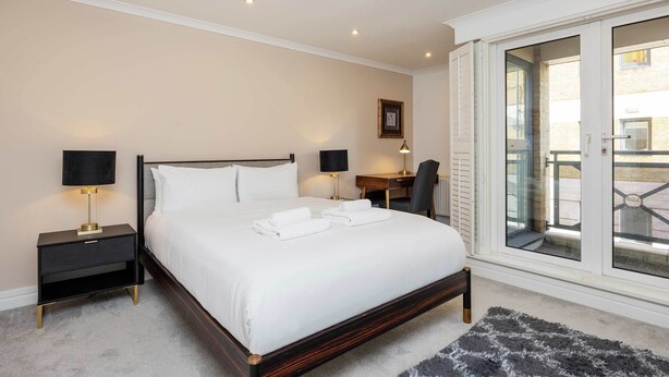 A neatly made bed with white linens, a dark wooden headboard, and two bedside tables with lamps. - At Home in Marylebone (London)